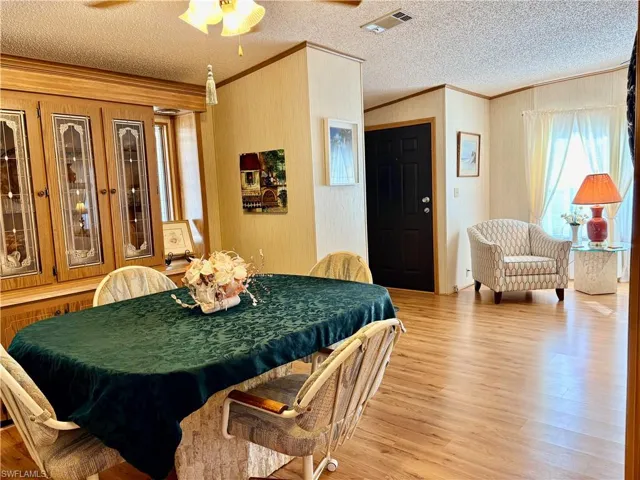 Dining space featuring ornamental molding, light wood-style floors, a ceiling fan, and a textured ceiling