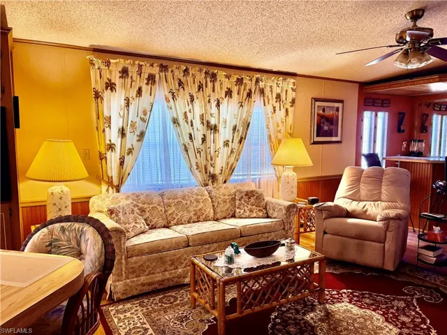 Living room with wooden walls, wainscoting, crown molding, ceiling fan, and a textured ceiling