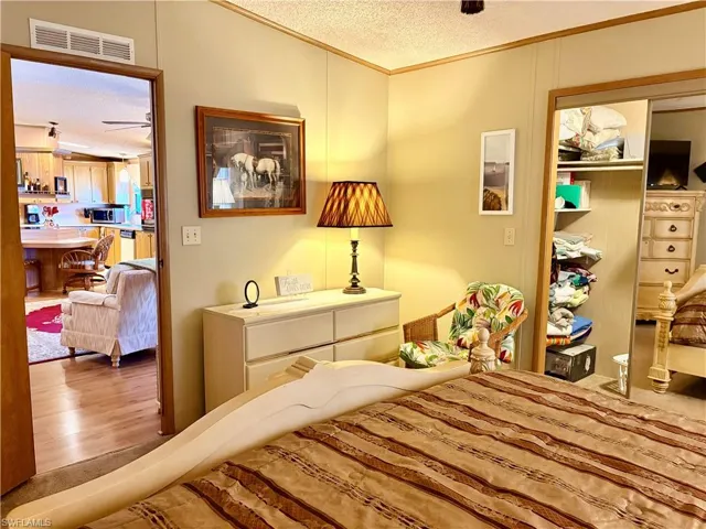 Bedroom with a textured ceiling, crown molding, a closet, wood finished floors, and a ceiling fan