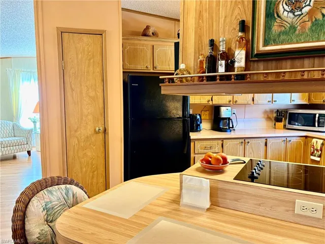 Kitchen featuring light countertops, black appliances, open shelves, and light wood finish cabinetry