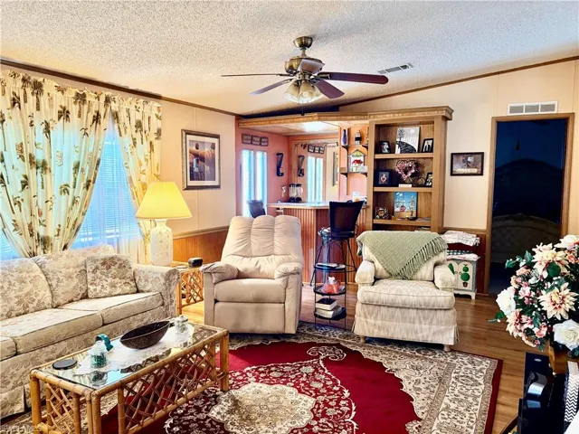 Living room featuring crown molding, a wainscoted wall, a textured ceiling, ceiling fan, and wooden walls