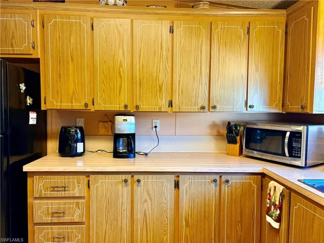Kitchen with light countertops, stainless steel microwave, freestanding refrigerator, and wood finish cabinets