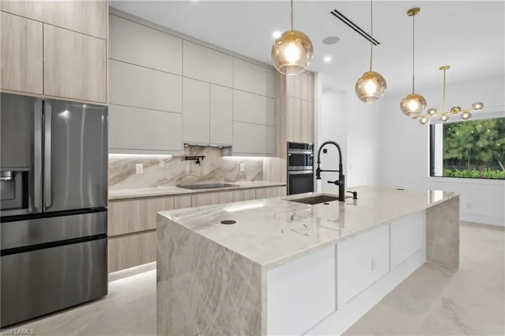 Kitchen with stainless steel refrigerator with ice dispenser, light stone countertops, light brown cabinets, hanging light fixtures, and recessed lighting