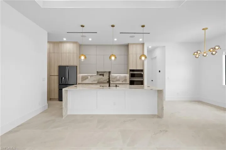 Kitchen featuring modern cabinets, light stone counters, decorative light fixtures, black fridge with ice dispenser, and recessed lighting