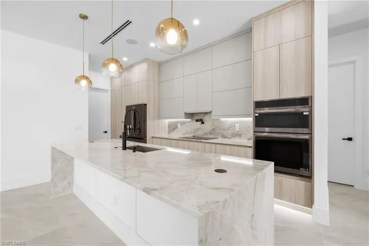 Kitchen featuring light brown cabinetry, modern cabinets, light stone countertops, backsplash, and decorative light fixtures