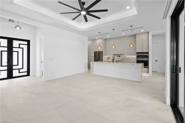 Kitchen with open floor plan, a center island with sink, pendant lighting, modern cabinets, and light stone countertops