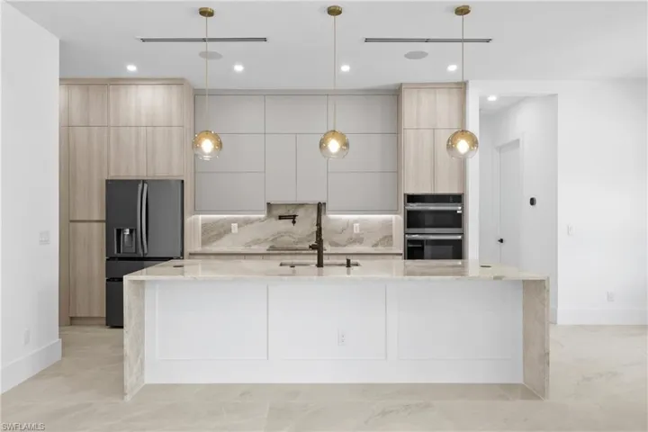Kitchen featuring light stone countertops, light brown cabinets, modern cabinets, black appliances, and recessed lighting