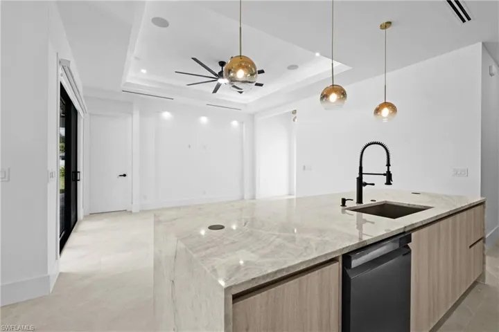 Kitchen featuring light stone counters, pendant lighting, light brown cabinets, stainless steel dishwasher, and modern cabinets