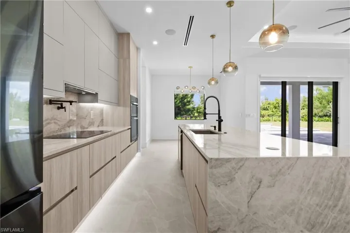 Kitchen featuring freestanding refrigerator, light stone countertops, hanging light fixtures, recessed lighting, and a large island with sink