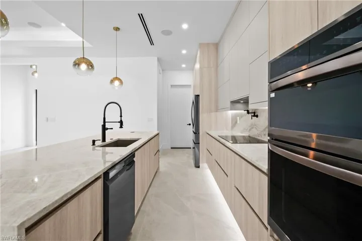 Kitchen with light brown cabinetry, black appliances, light stone countertops, and recessed lighting