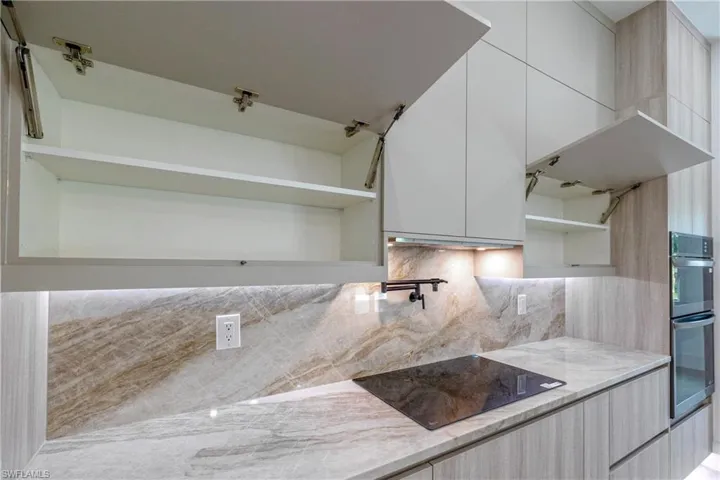 Kitchen featuring black electric stovetop, light stone counters, stainless steel double oven, open shelves, and modern cabinets