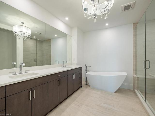 Primary Bathroom in the Primary Suite features dual sinks with standalone tub, walk-in shower, and upscale features and lighting.