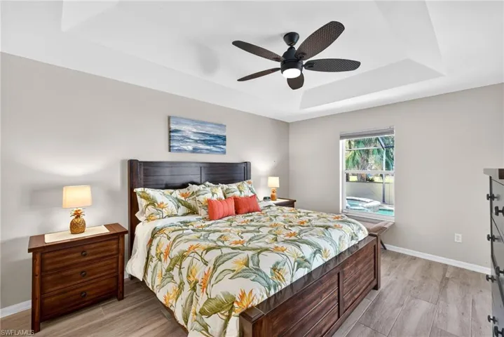 Bedroom featuring a raised ceiling, light wood-style floors, and ceiling fan