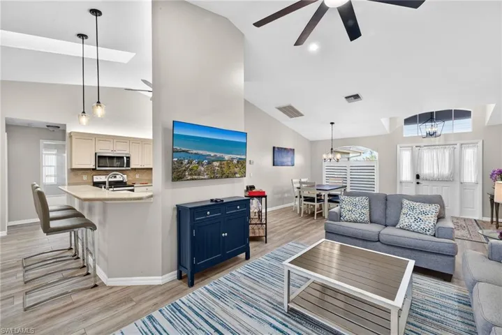 Living room with ceiling fan, high vaulted ceiling, a skylight, a chandelier, and light wood-style floors