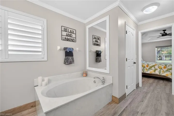 Ensuite bathroom with a garden tub, light wood finished floors, ceiling fan, and ornamental molding