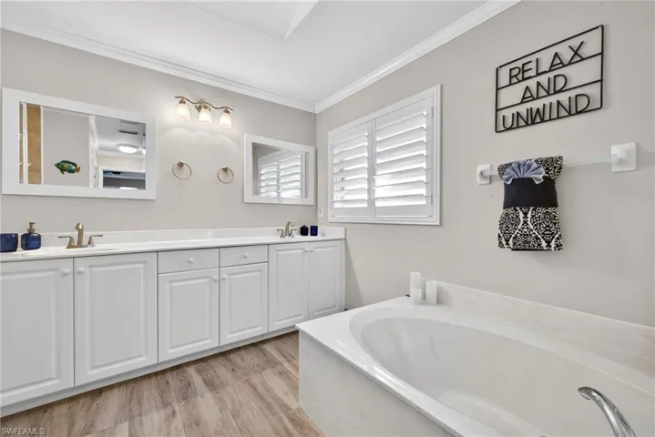 Full bath featuring double vanity, crown molding, light wood finished floors, and a garden tub