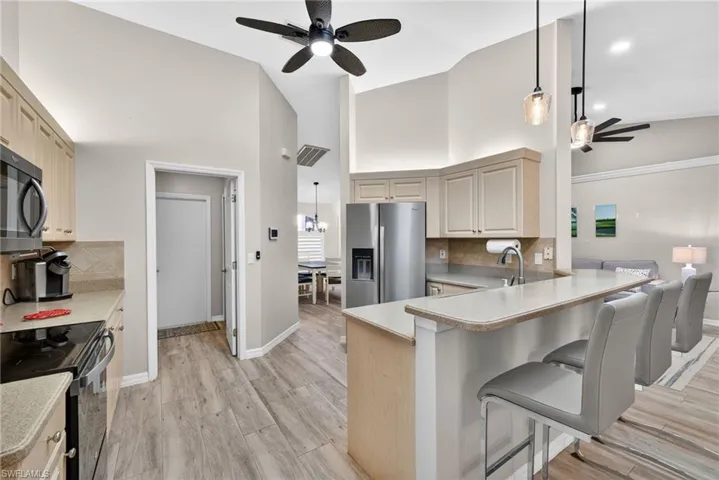 Kitchen featuring decorative backsplash, ceiling fan, decorative light fixtures, a breakfast bar area, and black appliances
