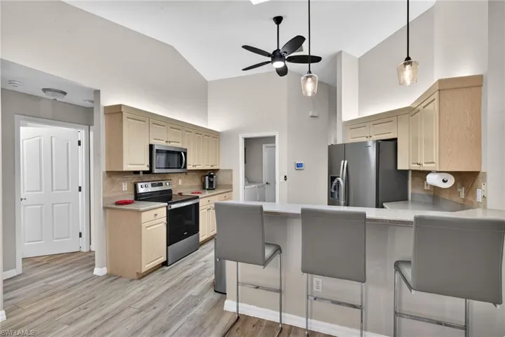 Kitchen featuring appliances with stainless steel finishes, a kitchen bar, decorative backsplash, light brown cabinetry, and high vaulted ceiling