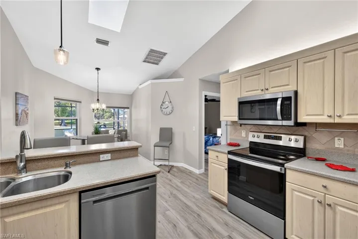 Kitchen with appliances with stainless steel finishes, vaulted ceiling, light brown cabinets, and a skylight
