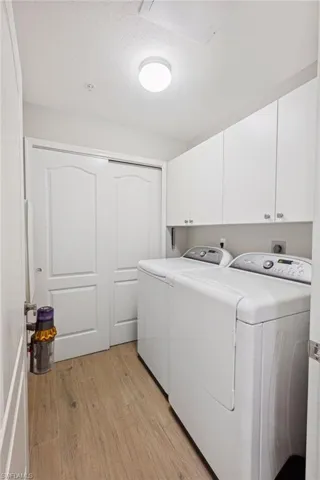 Laundry area with light wood-type flooring, independent washer and dryer, a textured ceiling, and cabinet space