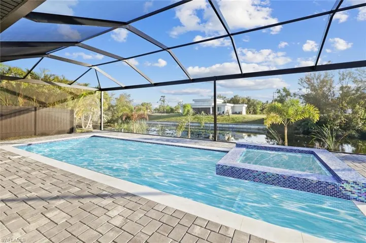 View of swimming pool with a lanai, a water view, and an in ground hot tub