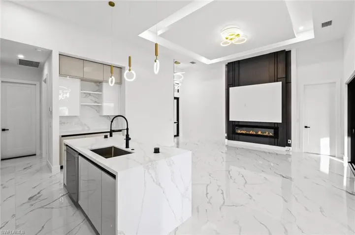 Kitchen with pendant lighting, a raised ceiling, sink, light stone countertops, and a fireplace