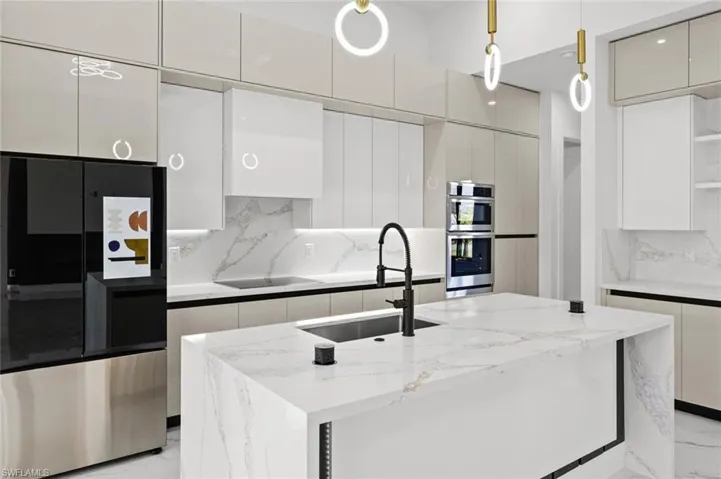 Kitchen featuring appliances with stainless steel finishes, tasteful backsplash, sink, pendant lighting, and a center island with sink