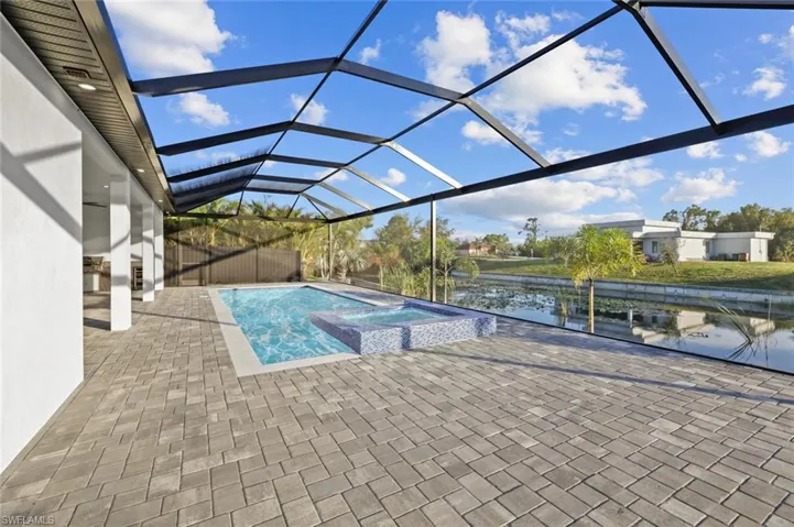 View of swimming pool with glass enclosure, an in ground hot tub, a water view, and a patio