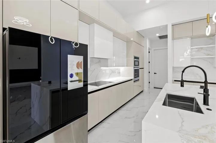 Kitchen with sink, black electric cooktop, decorative light fixtures, light stone counters, and white cabinetry