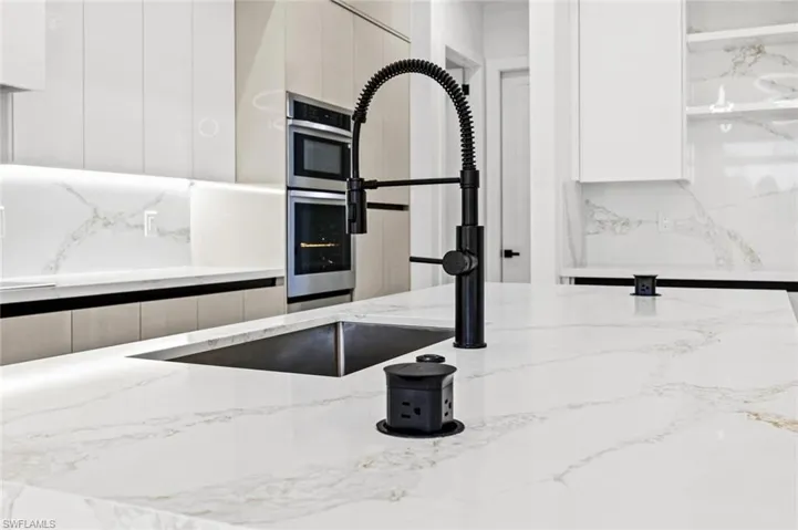 Interior details featuring light stone counters, sink, and tasteful backsplash