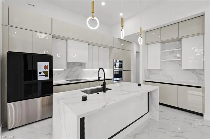 Kitchen with decorative backsplash, appliances with stainless steel finishes, light stone counters, sink, and hanging light fixtures