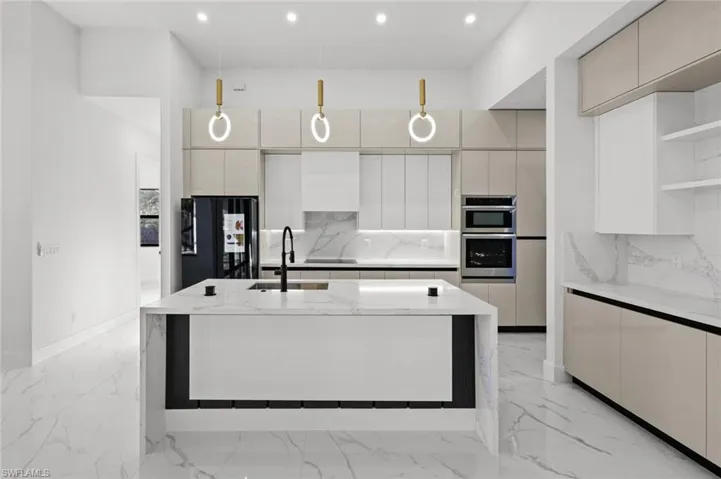Kitchen with black refrigerator, sink, hanging light fixtures, light stone counters, and stainless steel double oven