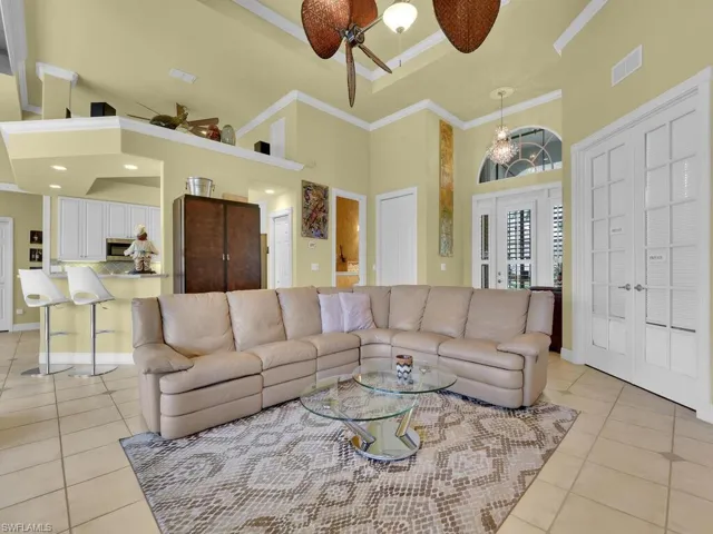 Tiled living room fan with notable chandelier, a high ceiling, and ornamental molding