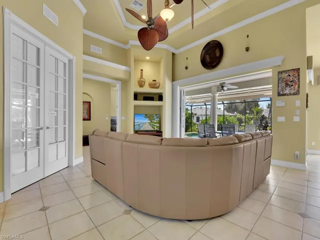 Living room with built in shelves, crown molding, ceiling fan, and French doors to the office