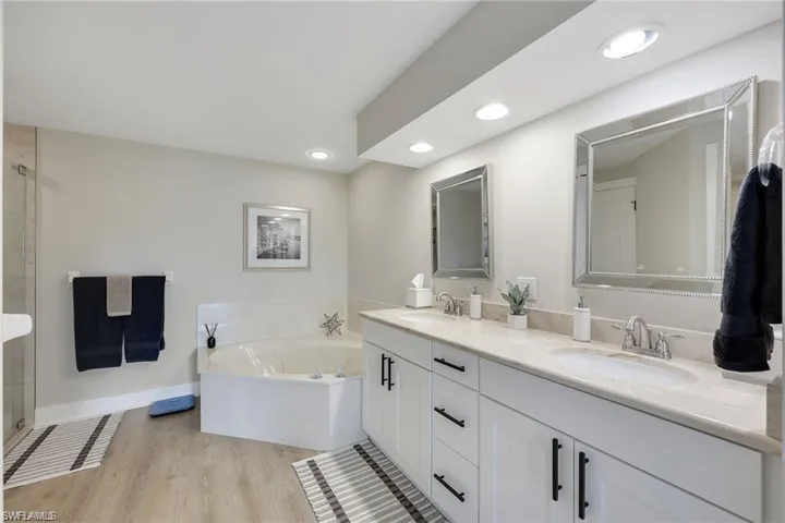 Full bath featuring a garden tub, double vanity, light wood-style floors, and a shower with shower door