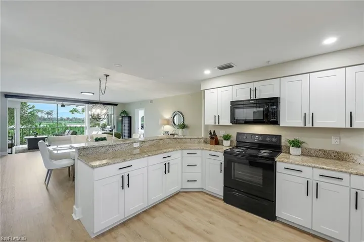 Kitchen featuring black appliances, a peninsula, white cabinetry, light wood-type flooring, and light stone countertops