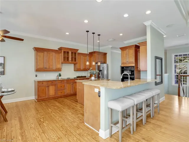 Kitchen featuring a breakfast bar area, high end refrigerator, light stone counters, kitchen peninsula, and light hardwood / wood-style flooring