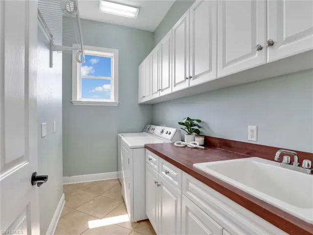 Laundry room featuring washer and dryer, sink, light tile patterned floors, and cabinets
