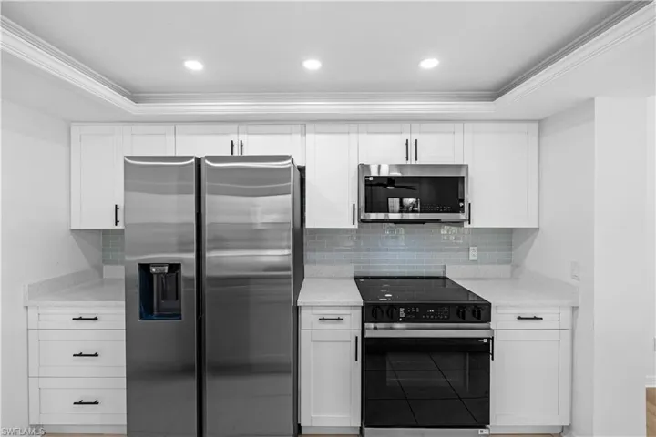 Kitchen with stainless steel appliances, crown molding, white cabinetry, light stone counters, and tasteful backsplash