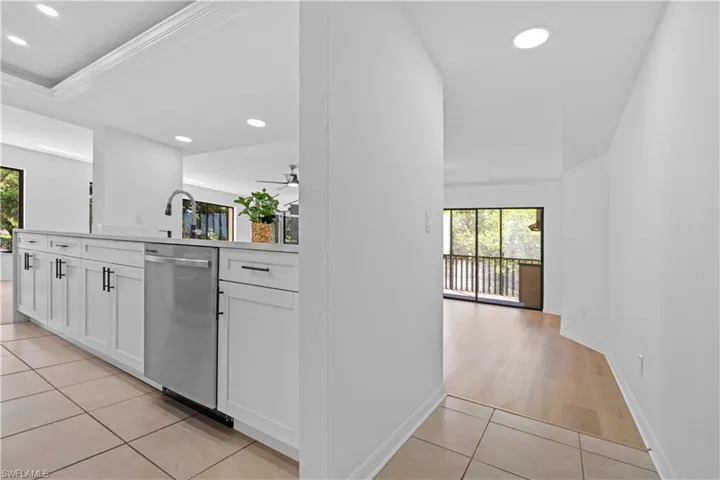 Kitchen with light tile patterned flooring, light countertops, white cabinets, stainless steel dishwasher, and plenty of natural light