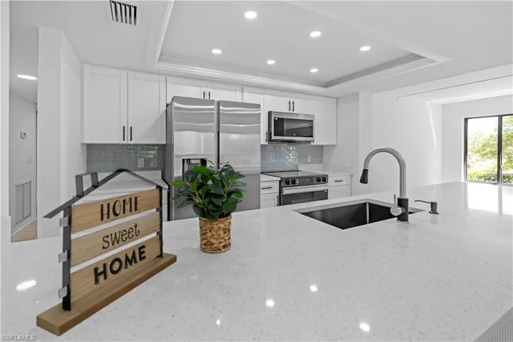Kitchen with white cabinetry, light stone counters, stainless steel appliances, recessed lighting, and ornamental molding