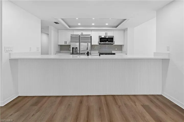 Kitchen featuring a peninsula, white cabinets, stainless steel appliances, a tray ceiling, and wood finished floors