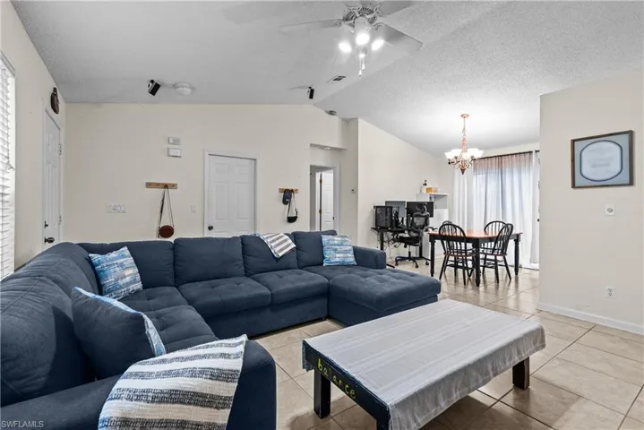 Tiled living room with a textured ceiling, lofted ceiling, and ceiling fan with notable chandelier