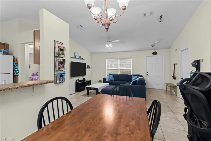 Dining area featuring ceiling fan with notable chandelier, vaulted ceiling, and light tile patterned floors