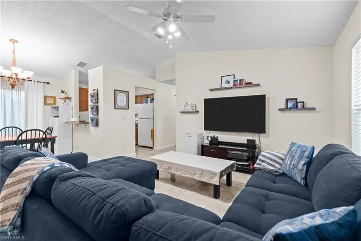 Tiled living room featuring lofted ceiling, a healthy amount of sunlight, ceiling fan with notable chandelier, and a textured ceiling