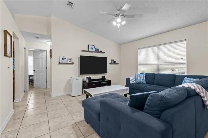 Living room with a textured ceiling, light tile patterned floors, vaulted ceiling, and ceiling fan