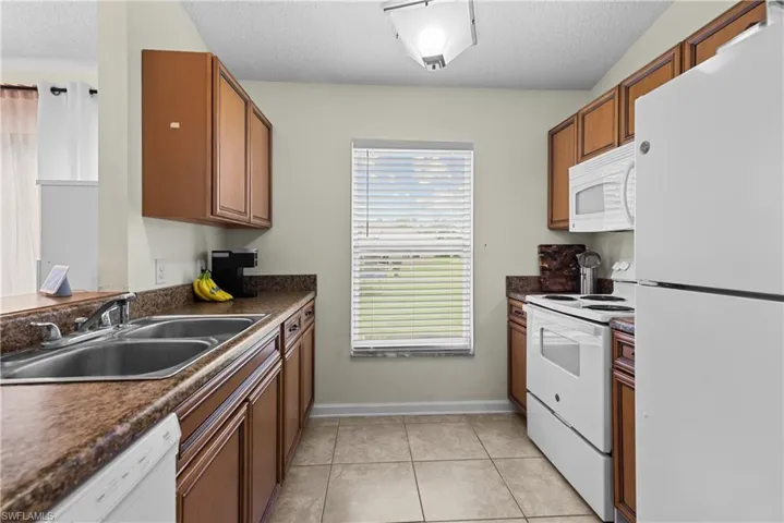 Kitchen featuring sink, a textured ceiling, white appliances, and light tile patterned floors
