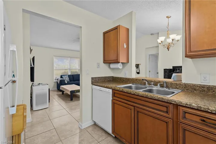Kitchen with white appliances, light tile patterned floors, a textured ceiling, an inviting chandelier, and sink
