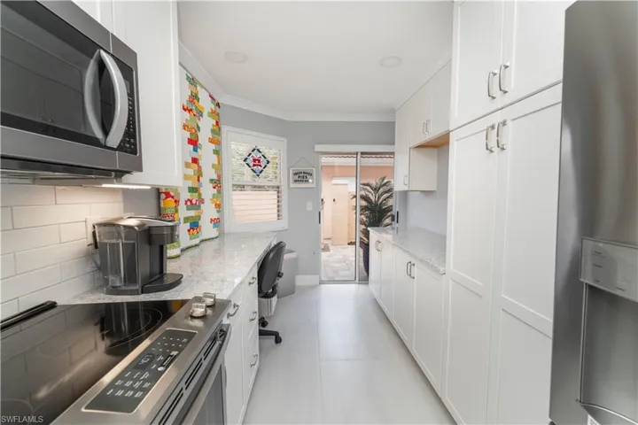 Kitchen with stainless steel appliances, white cabinetry, backsplash, crown molding, and light stone countertops
