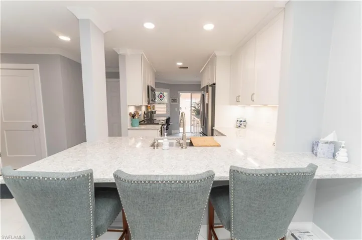Kitchen featuring a peninsula, white cabinetry, recessed lighting, a breakfast bar, and crown molding